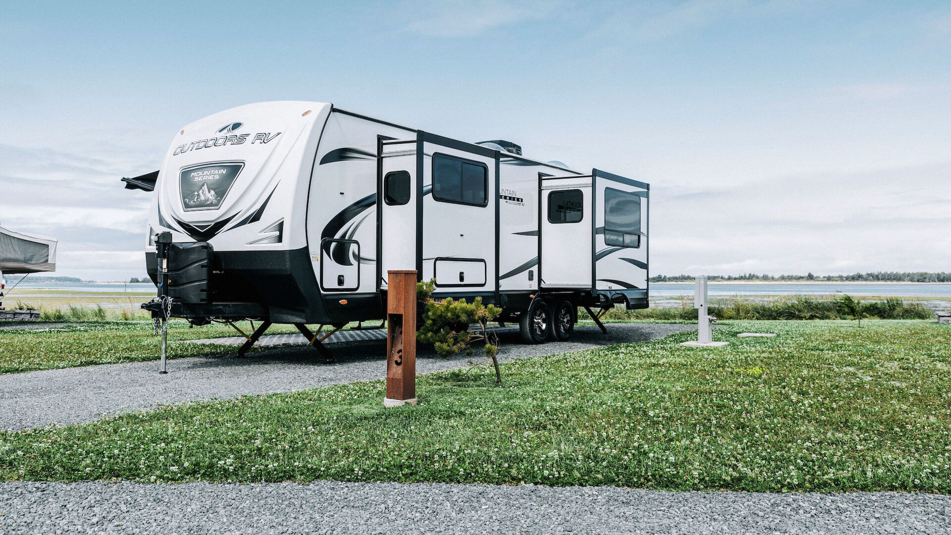 A large RV parked on a grassy area near a water source, with a cloudy sky in the background.