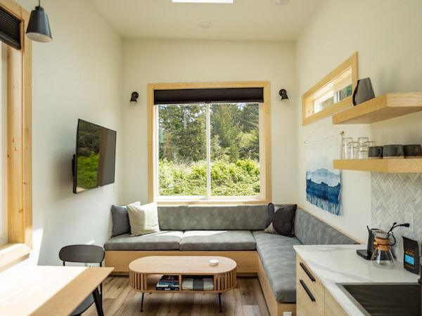 A cozy kitchen and living area with modern furnishings, a skylight, large window, seating, a table, and wall-mounted TV.