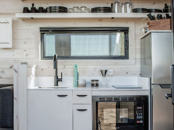 A compact kitchen with white cabinetry, a sink, stove, and a mini-fridge. Shelves hold cookware and utensils above. Cozy and efficient design.