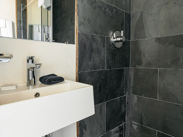 A modern bathroom features a sink with exposed plumbing and a shower with dark tile walls and a pebble floor.
