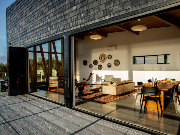 A modern open living and dining space with large glass doors leading to a wooden deck, featuring stylish furniture and wall decorations.