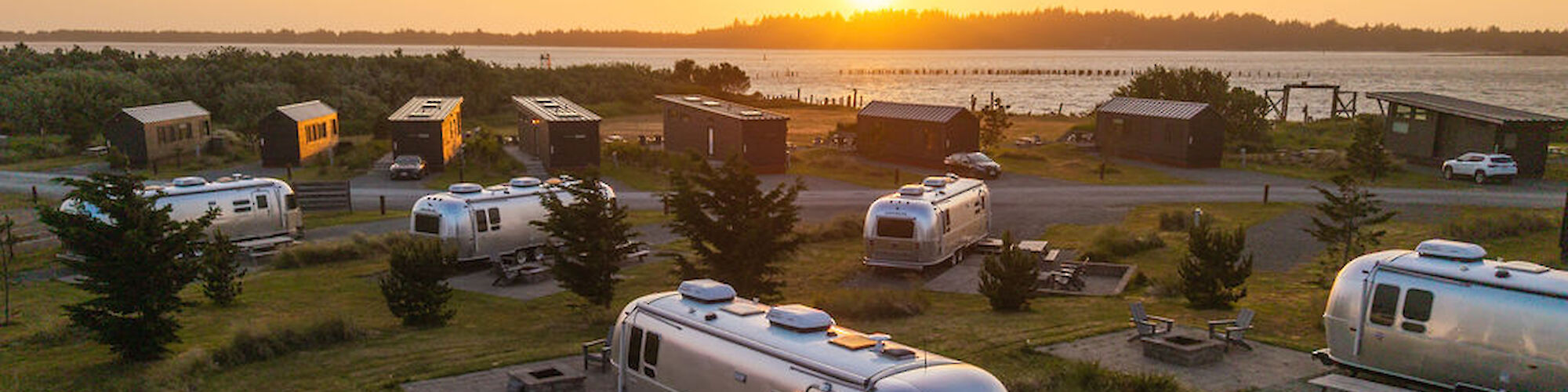 A scenic view of several Airstream trailers parked near each other with a beautiful sunset in the background, creating a serene setting.