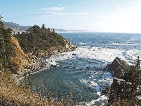 A scenic coastal view with rocky cliffs, waves crashing below, and a clear blue sky above the ocean horizon.