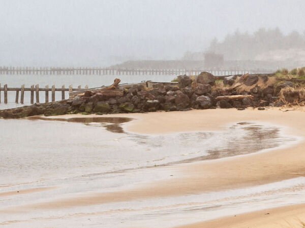 A serene beach scene with calm waves lapping at the shore, rocks, and a distant pier shrouded in a misty atmosphere.