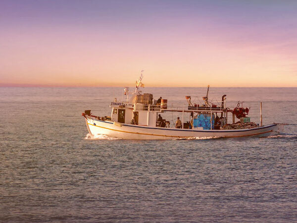 A fishing boat sails on calm waters under a colorful twilight sky, creating a serene and picturesque scene.