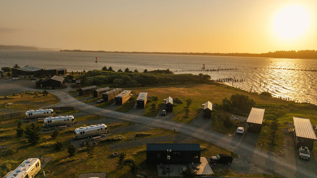 A scenic view of a lakeside RV park at sunset, with several trailers and cabins along a winding road near the water.