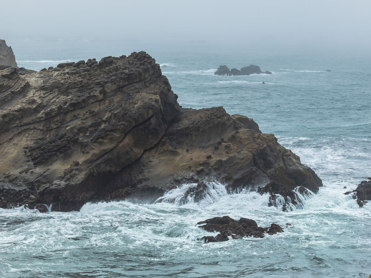 Rocky coastline with waves crashing against the cliffs under a cloudy sky.