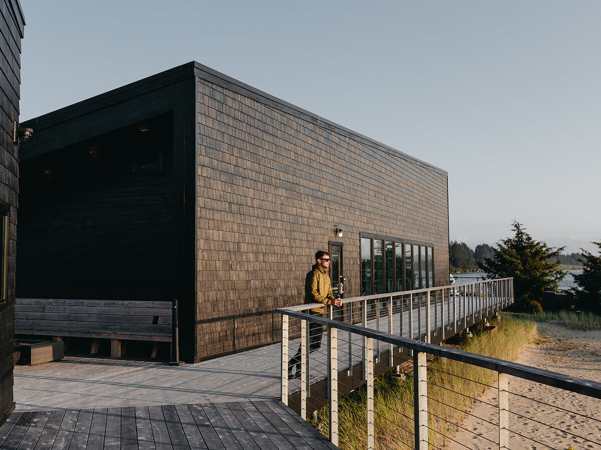 A modern brick building with a long ramp and railing, a person standing near the entrance, open space and grassy area nearby, sunny day on the Southern Oregon Coast.