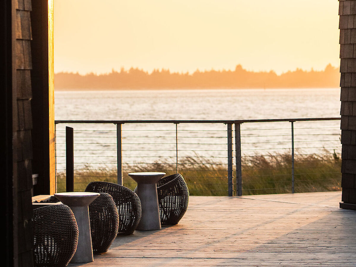A serene outdoor setting on the Southern Oregon Coast with water in the background and seating, bathed in a warm sunset glow.