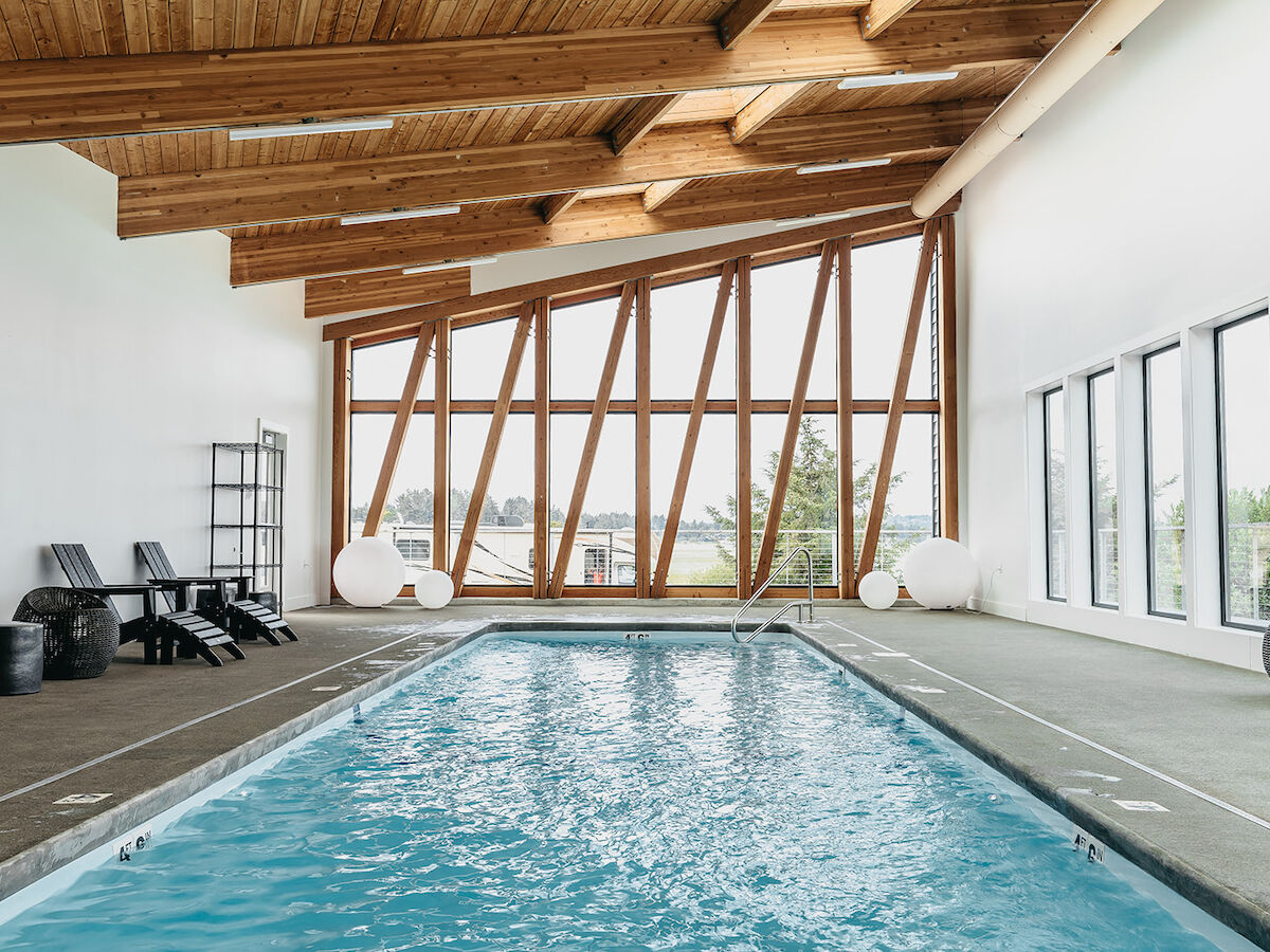 An indoor pool with modern wooden beams, large windows, and lounge chairs around, creating a bright and open atmosphere.