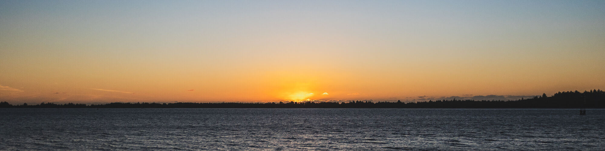 A tranquil sunset over a calm body of water with a clear sky and distant horizon.