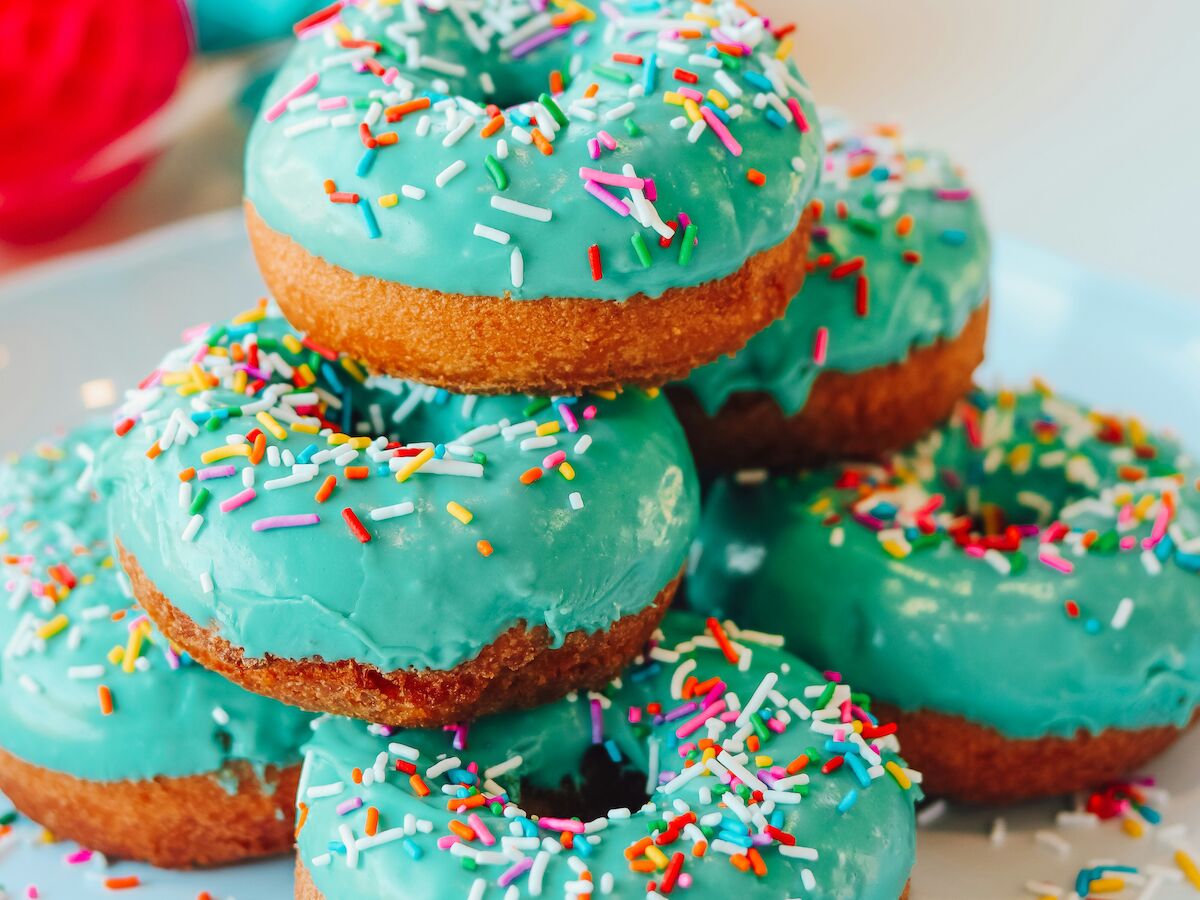 A stack of donuts with blue icing and colorful sprinkles, surrounded by colorful, blurred decorations in the background.