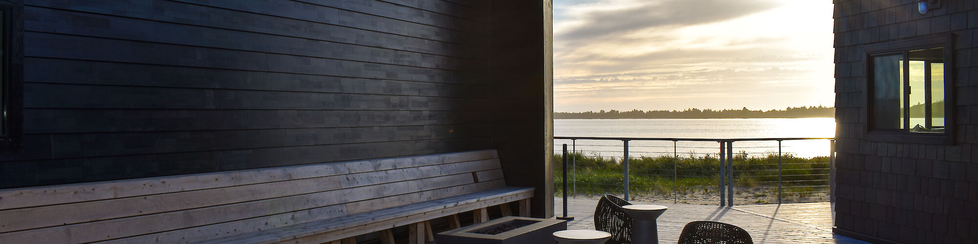 A modern outdoor terrace with seating, overlooking a body of water during sunset.