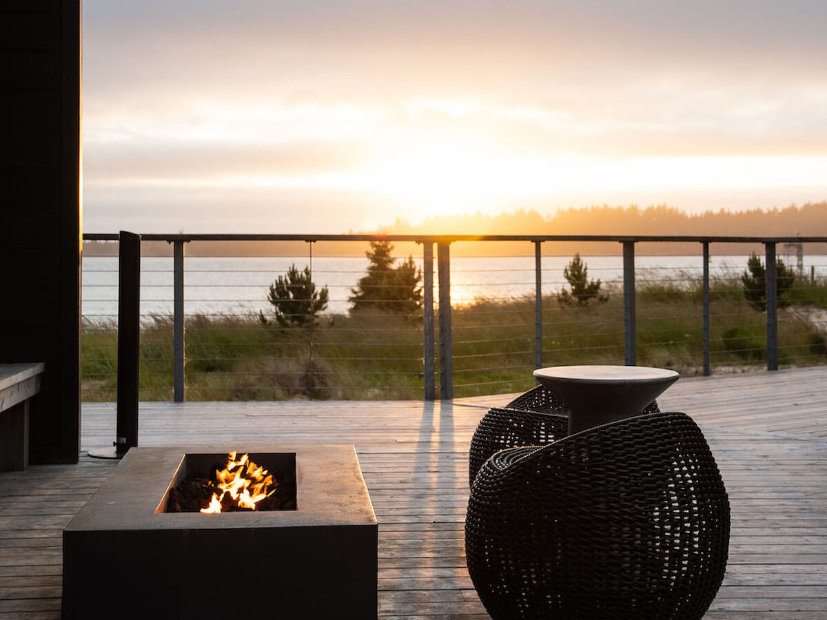 A patio with a fire pit and outdoor seating overlooks a scenic sunset by the bay in Southern Oregon, framed by a railing.