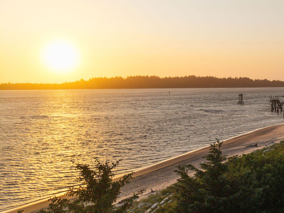 A sunset over a large body of water with a sandy beach in the foreground and trees along the shoreline of Bay Point Landing.