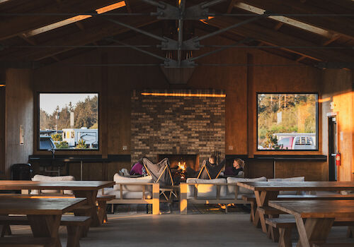 A cozy indoor space with a fireplace, wooden tables, and large windows, offering a warm and inviting atmosphere.