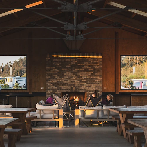 A cozy indoor space with a fireplace, wooden tables, and large windows, offering a warm and inviting atmosphere.