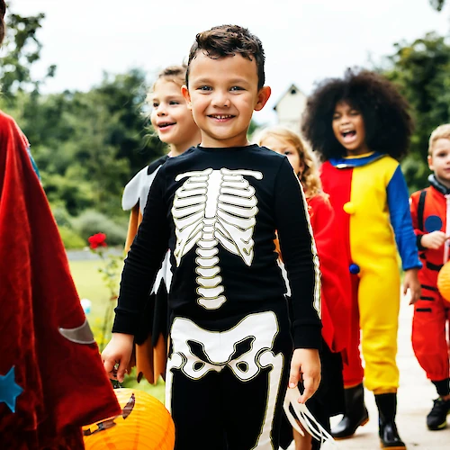 Children wearing costumes and holding pumpkin baskets while walking in a line outdoors.