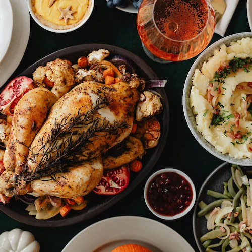 A Thanksgiving meal with roast chicken, mashed potatoes, green beans, cranberry sauce, and pumpkin soup is beautifully arranged.