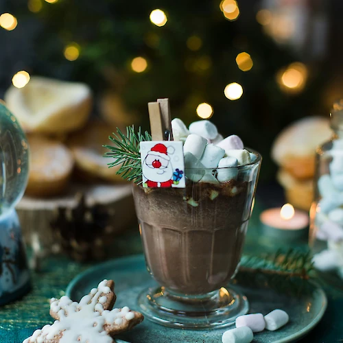A festive hot chocolate with marshmallows, cookie, and holiday decor, set against a warm, twinkling background.