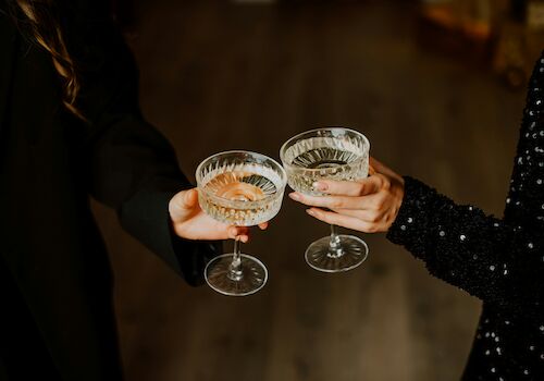 Two people clinking cocktails in coupe glasses, cheers moment, night out vibe.