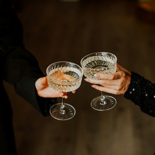 Two people clinking cocktails in coupe glasses, cheers moment, night out vibe.