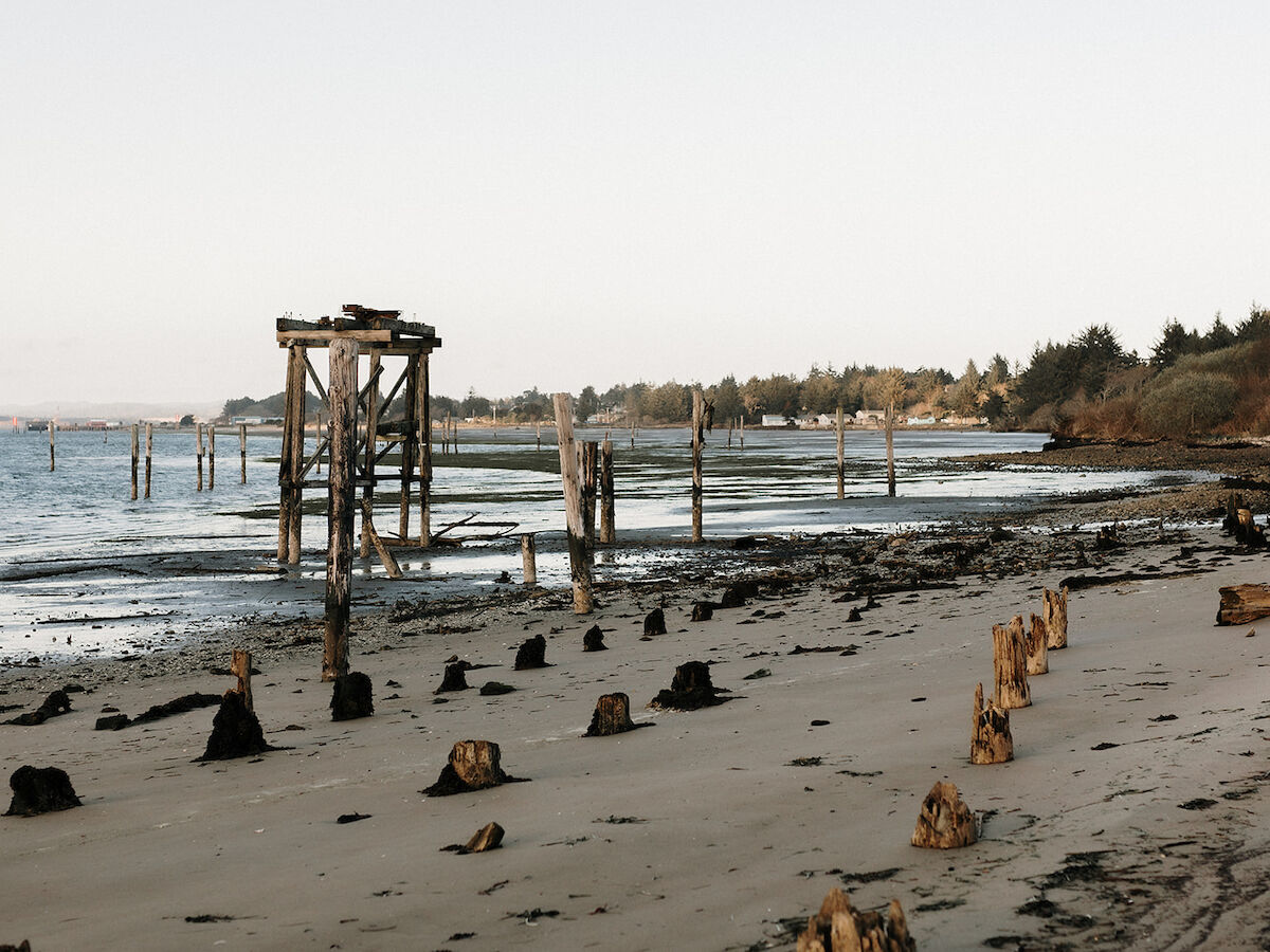 A deserted beach at low tide shows broken wooden pier remains and weathered posts along the shoreline.